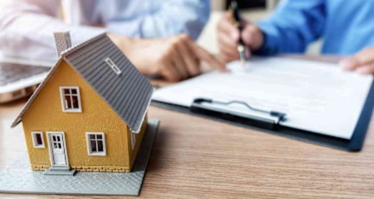 Miniature yellow house model on desk with two people reviewing documents and taking notes in background
