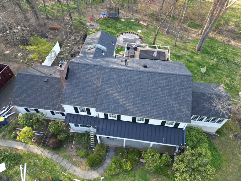 Aerial view of a modern black and white residential home with gray roof surrounded by tall trees and forest landscape