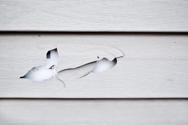 Torn white paint peeling off weathered wooden siding, showing damage and deterioration