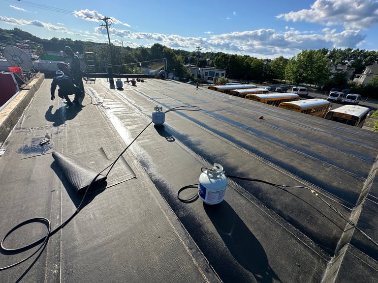 Workers applying waterproof membrane coating to a flat commercial roof during daytime construction