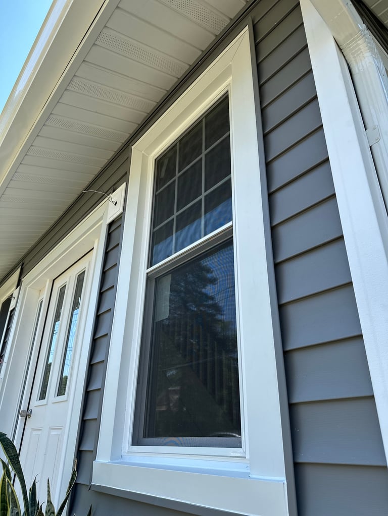 Modern house exterior with white trim windows and gray horizontal siding, clear blue sky visible