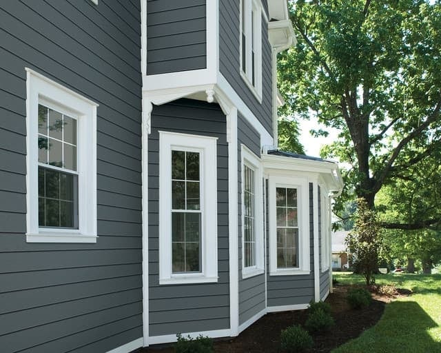 Modern gray and white house exterior with large windows and manicured landscaping on a sunny day